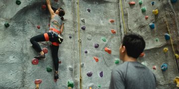 Back view of young female climbing wall while man writing results and watching