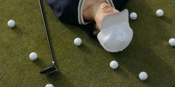 Asian woman in white cap lying on golf course with golf balls and club.